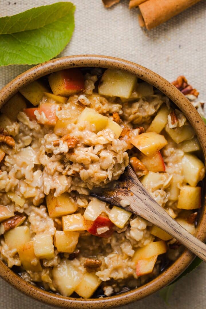 Apple cinnamon oatmeal being spooned out of a serving bowl, topped with sauteed apples.