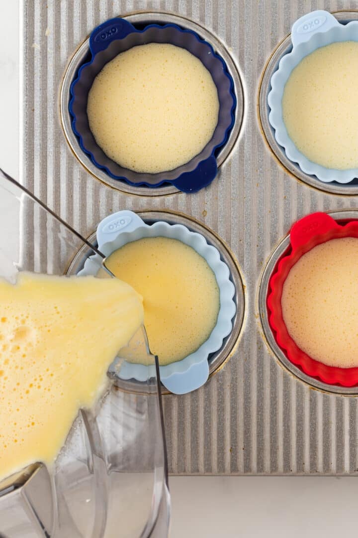 Egg bite batter being poured into silicone liners in a baking pan.