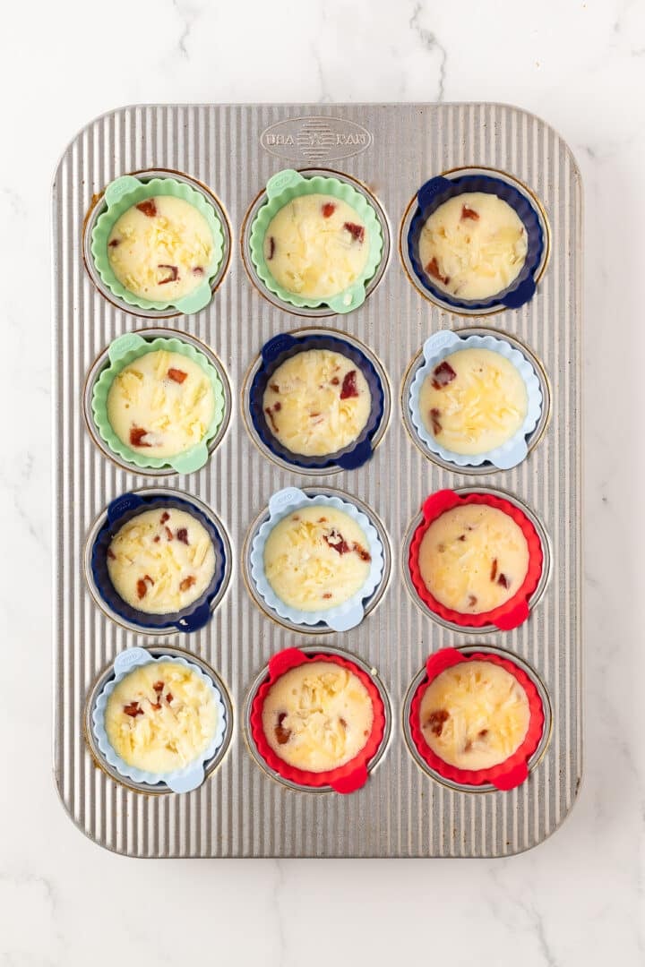 Bacon gruyere egg cups before baking, in a baking pan.