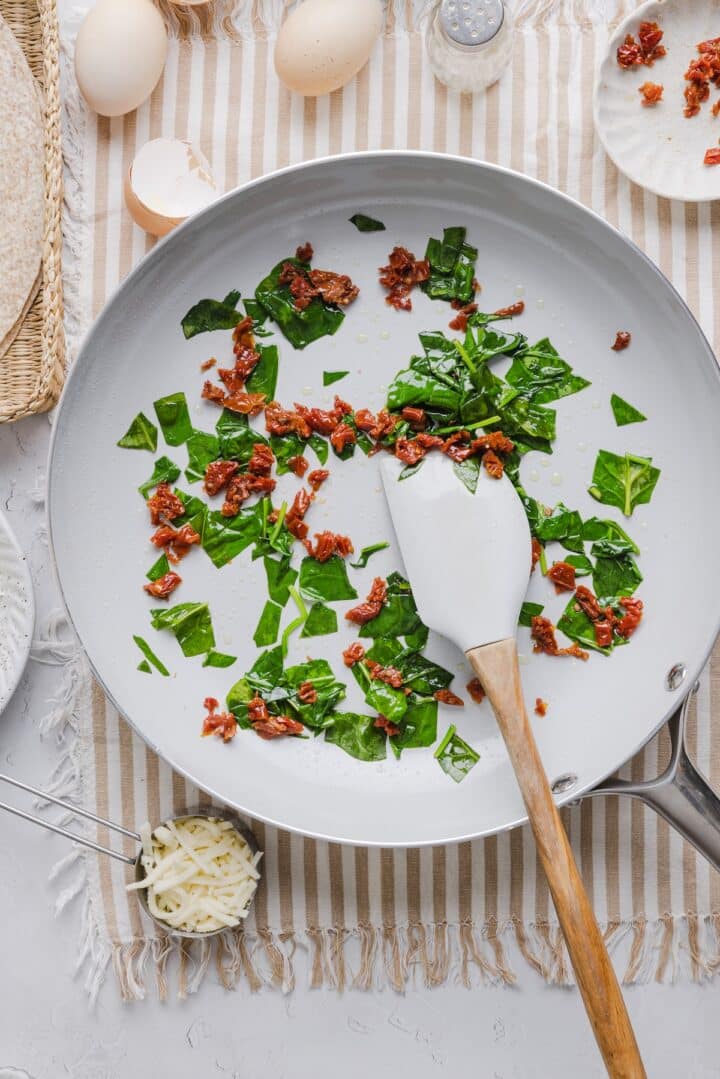 Spinach and sun dried tomatoes sauteed in a pan.