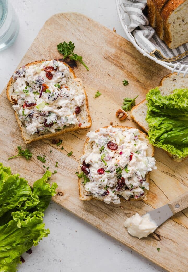 Cranberry pecan chicken salad on open-faced bread on a wooden cutting board.