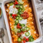 Easy chicken enchiladas in a white baking dish with sour cream and toppings.