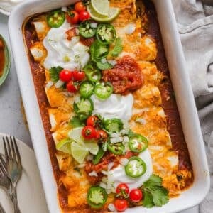 Easy chicken enchiladas in a white baking dish with sour cream and toppings.
