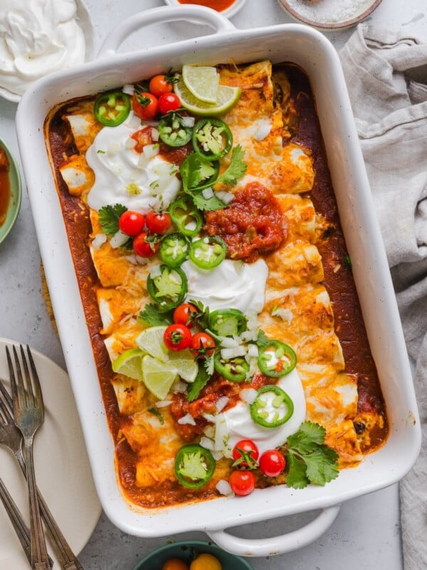 Easy chicken enchiladas in a white baking dish with sour cream and toppings.