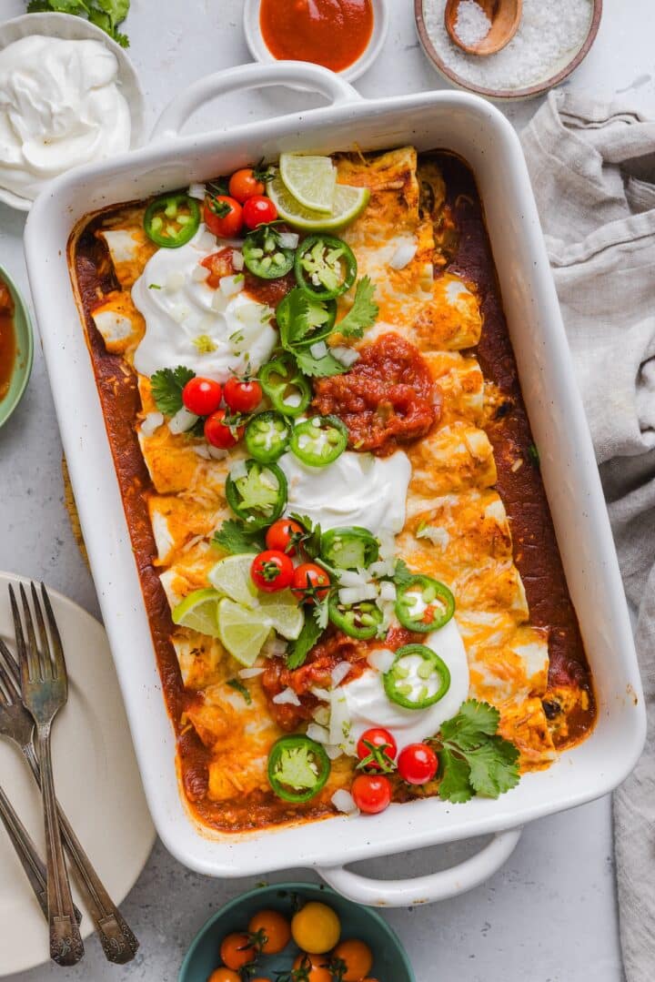 Easy chicken enchiladas in a white baking dish with sour cream and toppings.