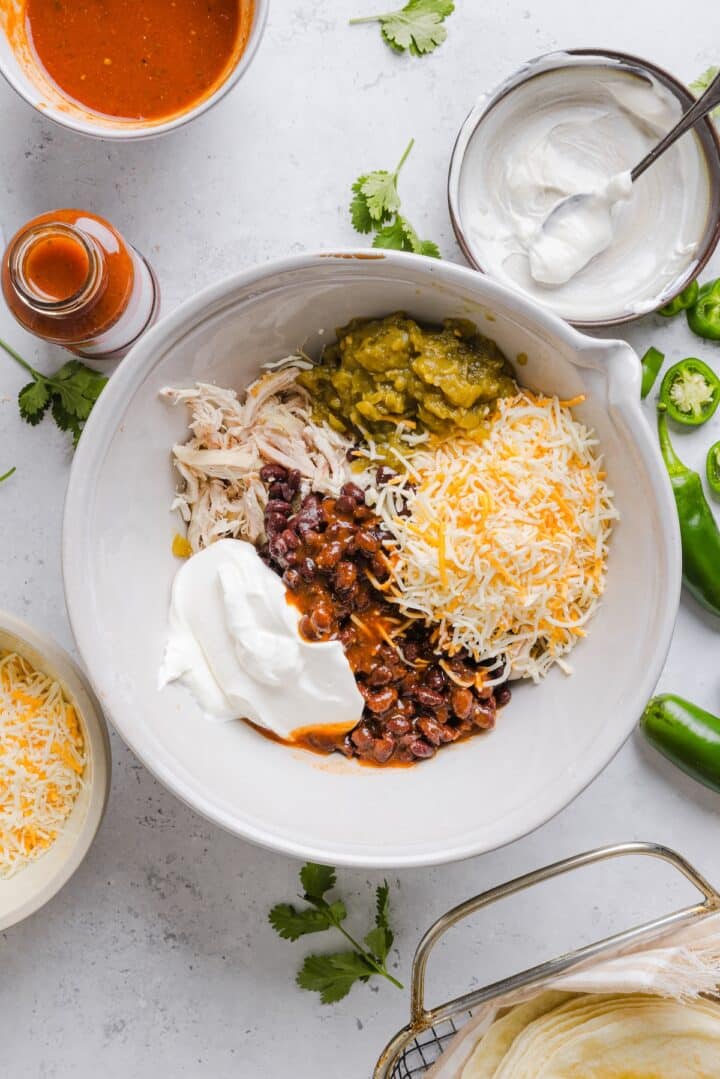 Ingredients for chicken enchilada filling in a large, white mixing bowl.