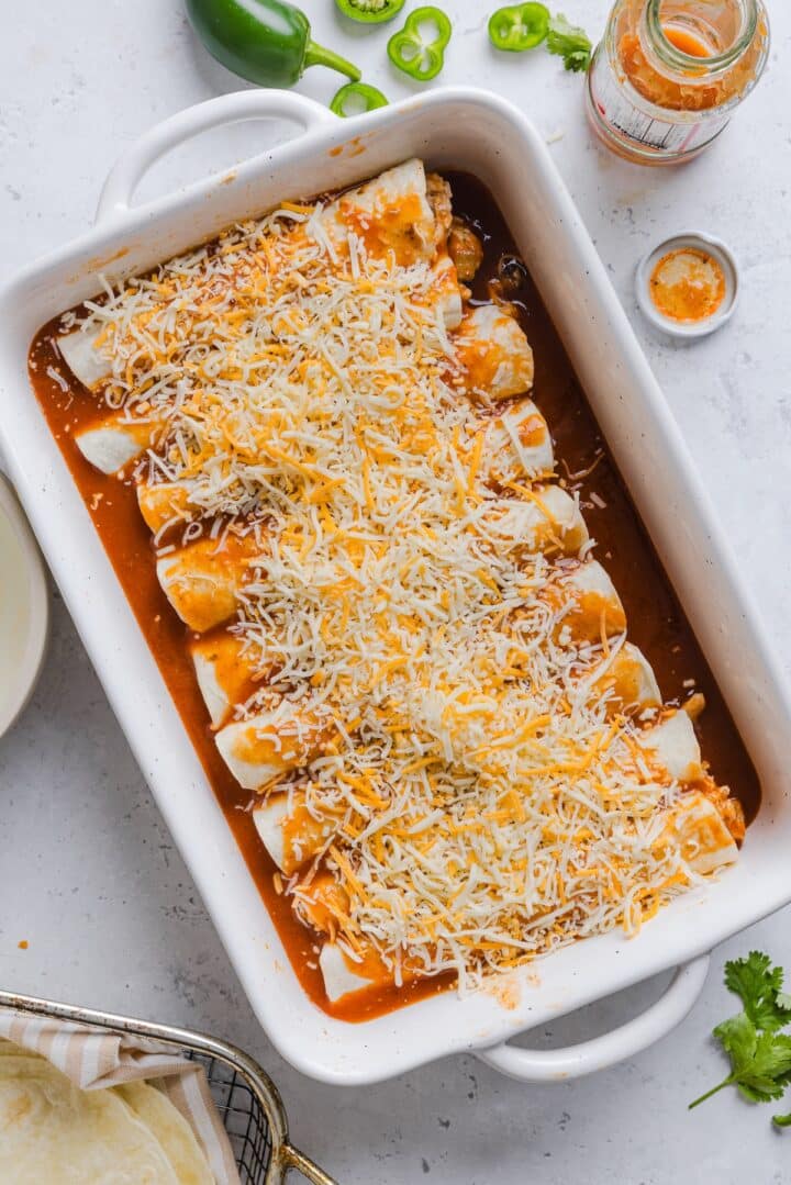 Easy chicken enchiladas topped with cheese in a white baking dish, raw.