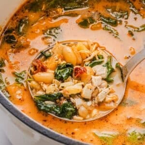 Marry be chicken soup in a large white Dutch oven with a vintage silver ladle.