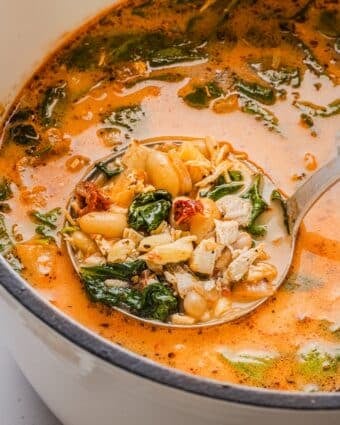 Marry be chicken soup in a large white Dutch oven with a vintage silver ladle.