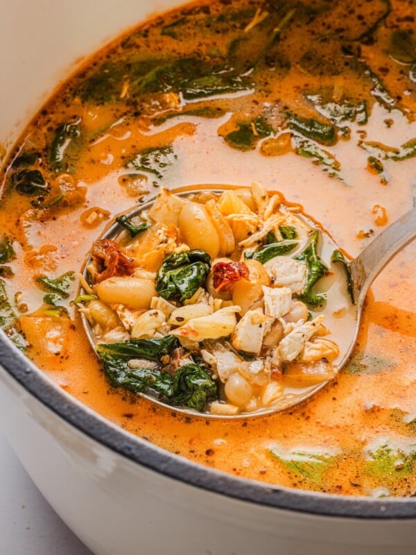 Marry be chicken soup in a large white Dutch oven with a vintage silver ladle.