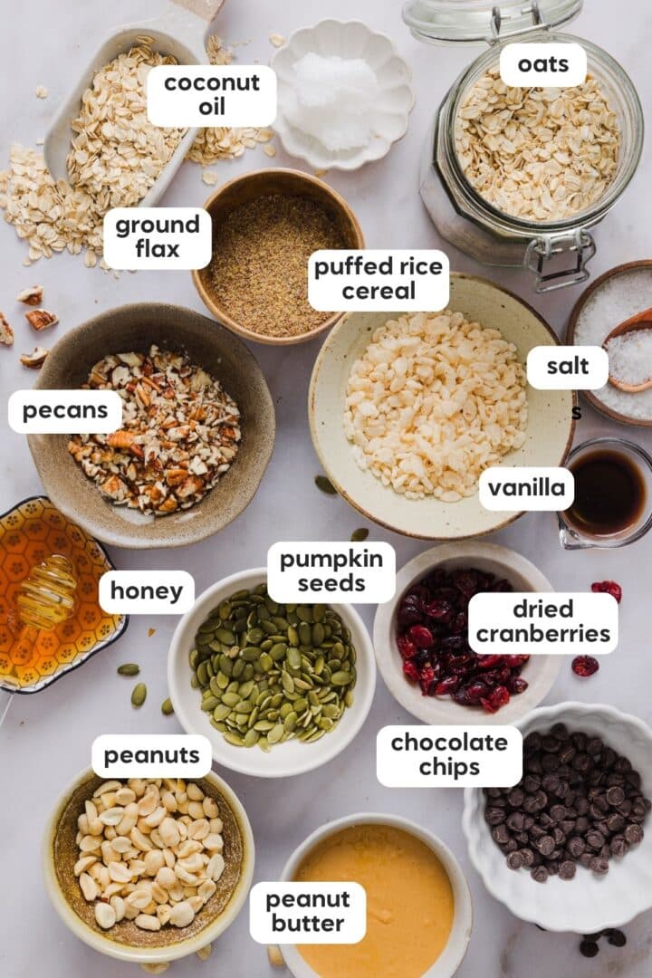 Ingredients for no-bake trail mix granola bars displayed in small bowls on a white kitchen counter.