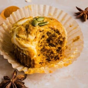 Pumpkin Oatmeal Muffin with cream cheese swirl in a paper muffin liner, on a marble counter.
