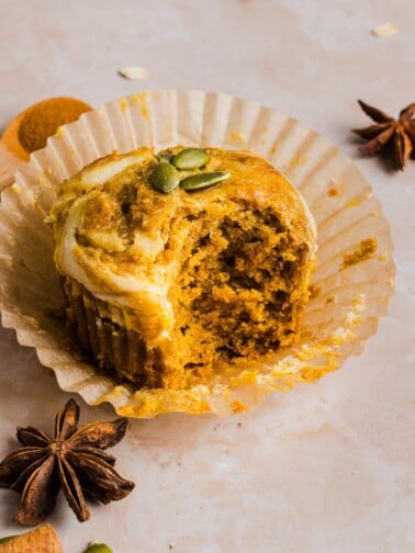 Pumpkin Oatmeal Muffin with cream cheese swirl in a paper muffin liner, on a marble counter.