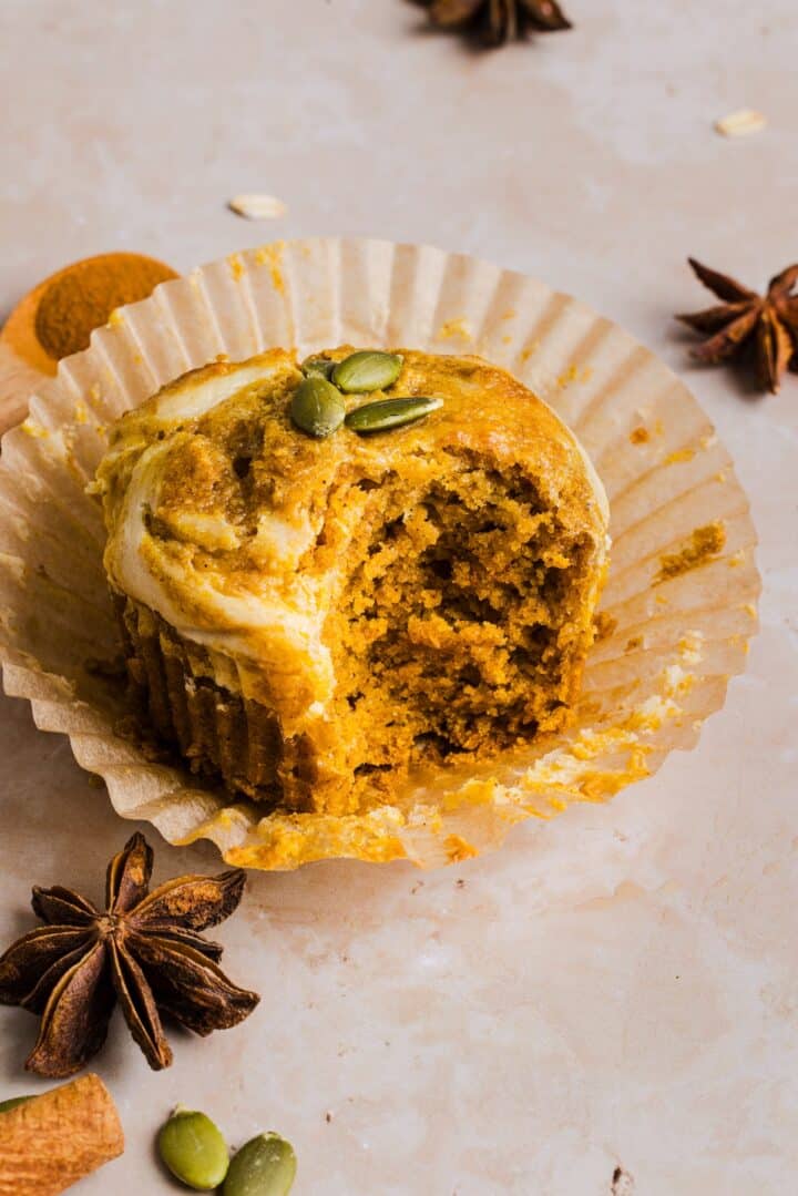 Pumpkin Oatmeal Muffin with cream cheese swirl in a paper muffin liner, on a marble counter.