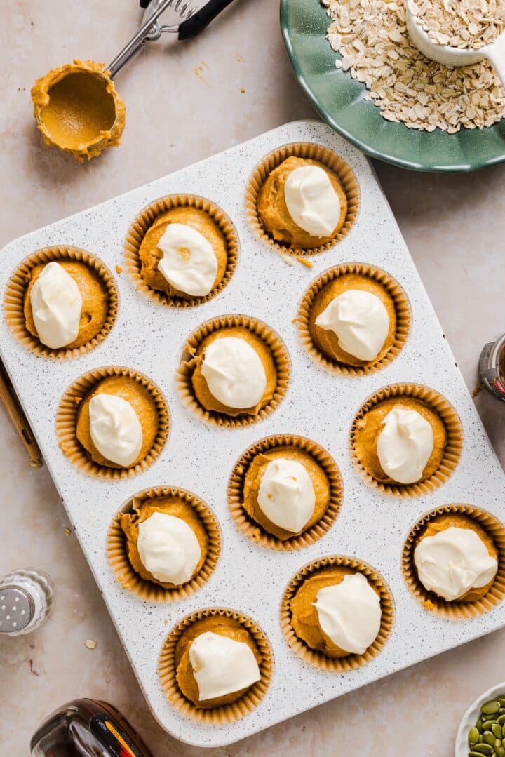 Pumpkin oatmeal muffins in a muffin tin, with cream cheese on top.