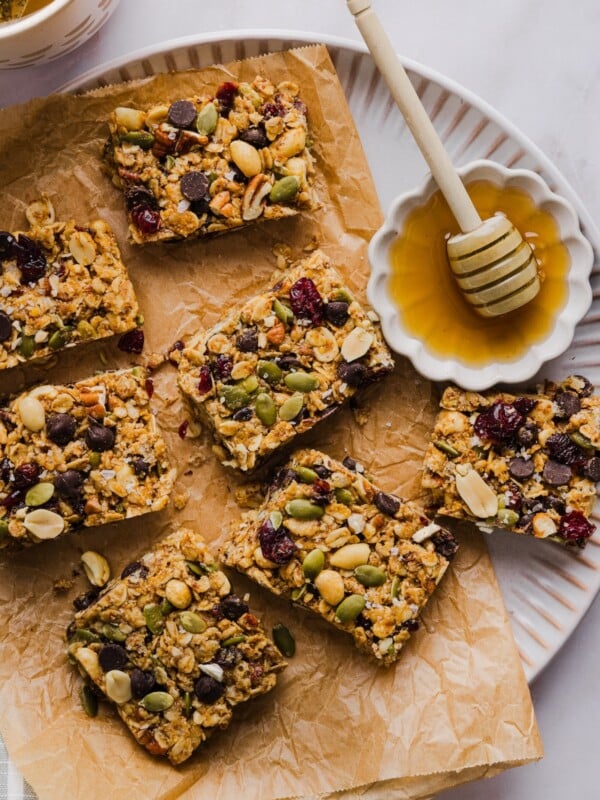 No-bake trail mix bars sliced and arranges on a parchment-lined plate with honey.