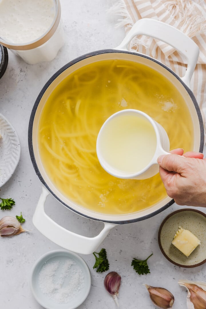 Spaghetti cooking in a large pot, reserving some pasta water in a measuring cup.