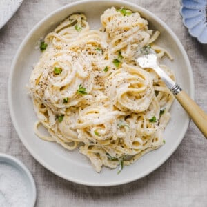 Cottage cheese alfredo pasta in a white, shallow bowl with a fork.