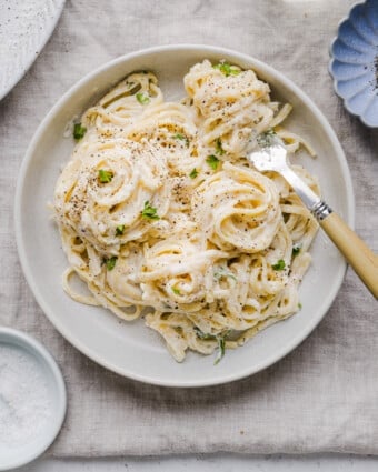 Cottage cheese alfredo pasta in a white, shallow bowl with a fork.
