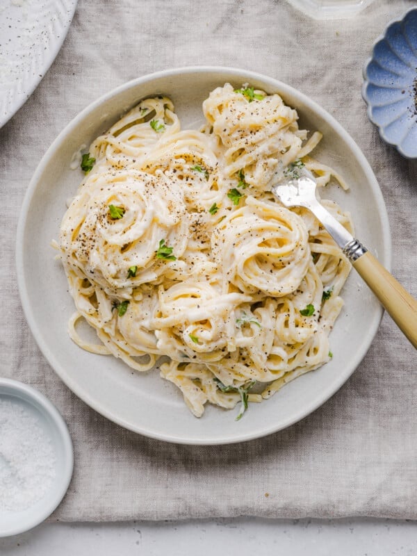 Cottage cheese alfredo pasta in a white, shallow bowl with a fork.