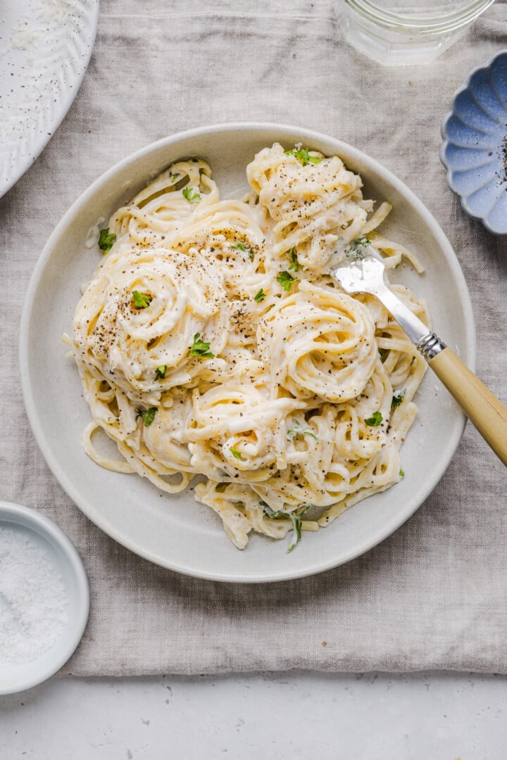 Cottage cheese alfredo pasta in a white, shallow bowl with a fork.