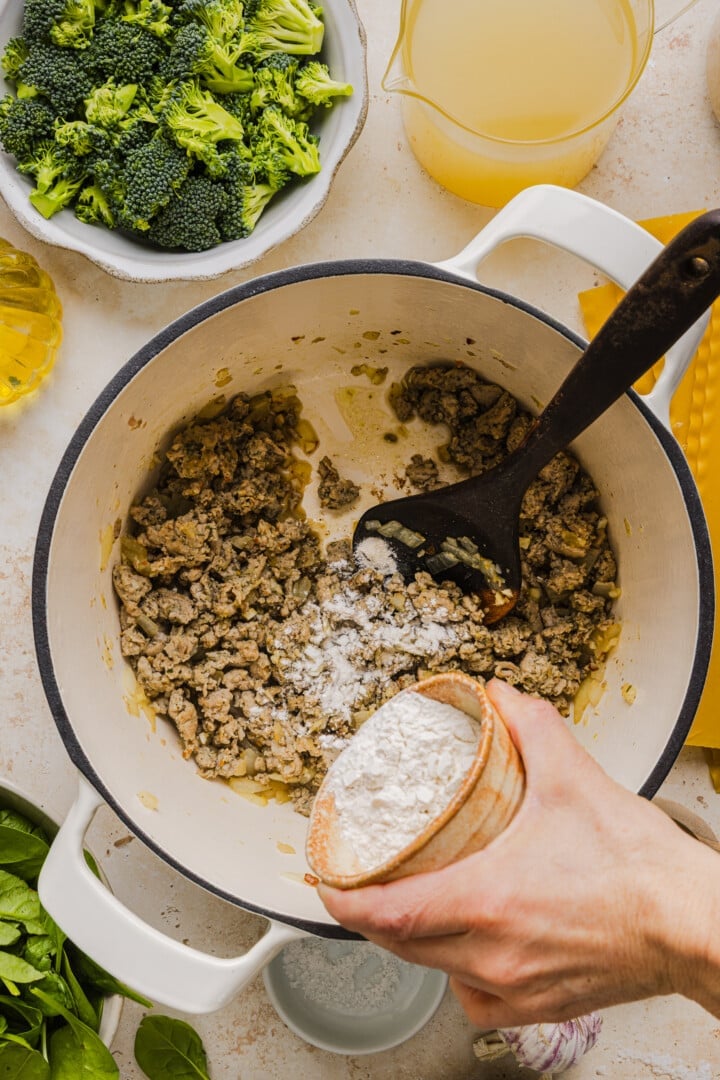 Flour being added to cooked ground chicken in a large pot.