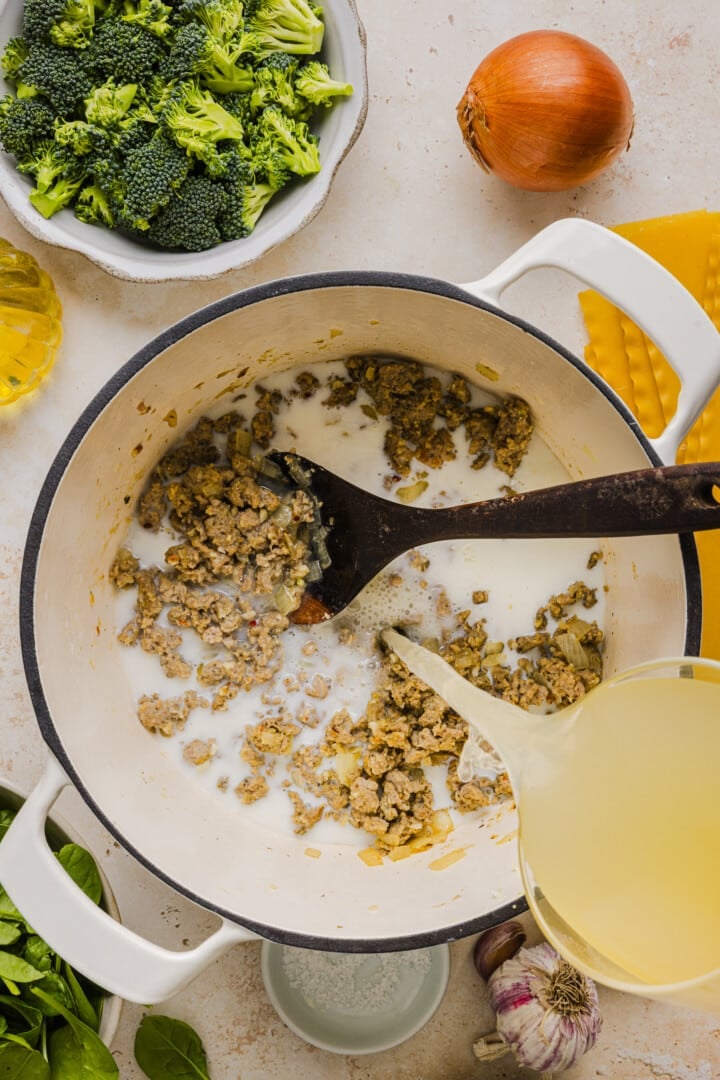 Milk and broth being added to soup in a large white pot.