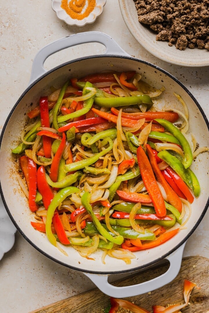 Sliced peppers and onions cooked in a large white pan.