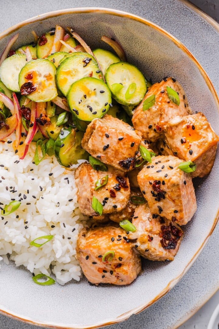 Bang bang salmon bites in a bowl with rice and cucumber salad