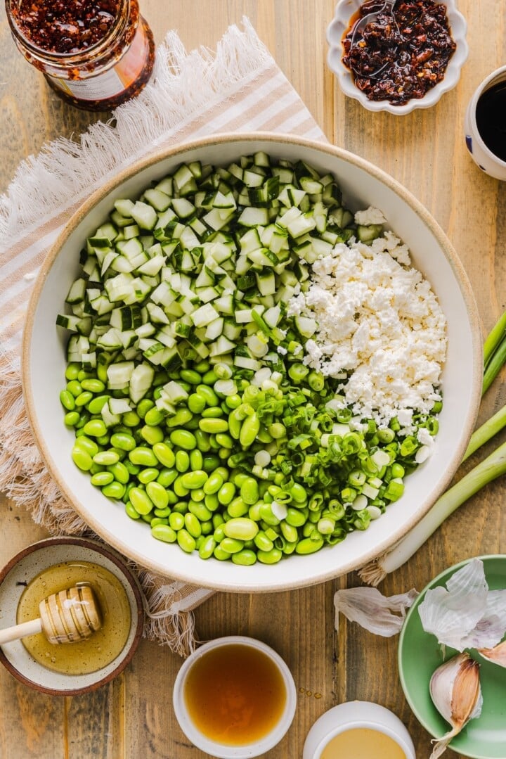 Cucumber edamame salad unmixed in a white serving bowl.