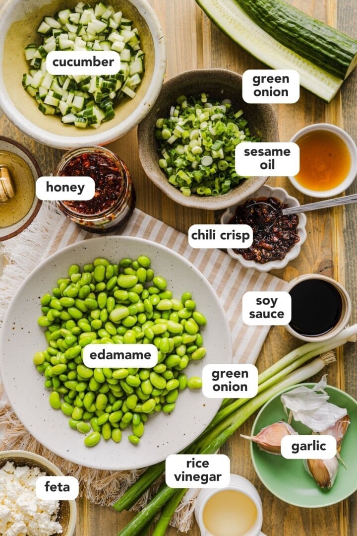 Ingredients for cucumber edamame salad displayed in small bowls on a kitchen counter.