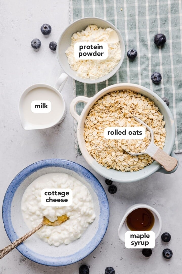 Ingredients for cottage cheese overnight oats displayed in small bowls on a grey marble counter.