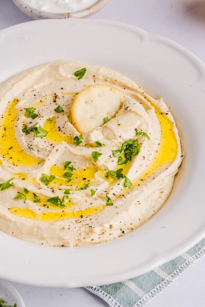High Protein hummus with cottage cheese displayed in a white bowl with pita chips.