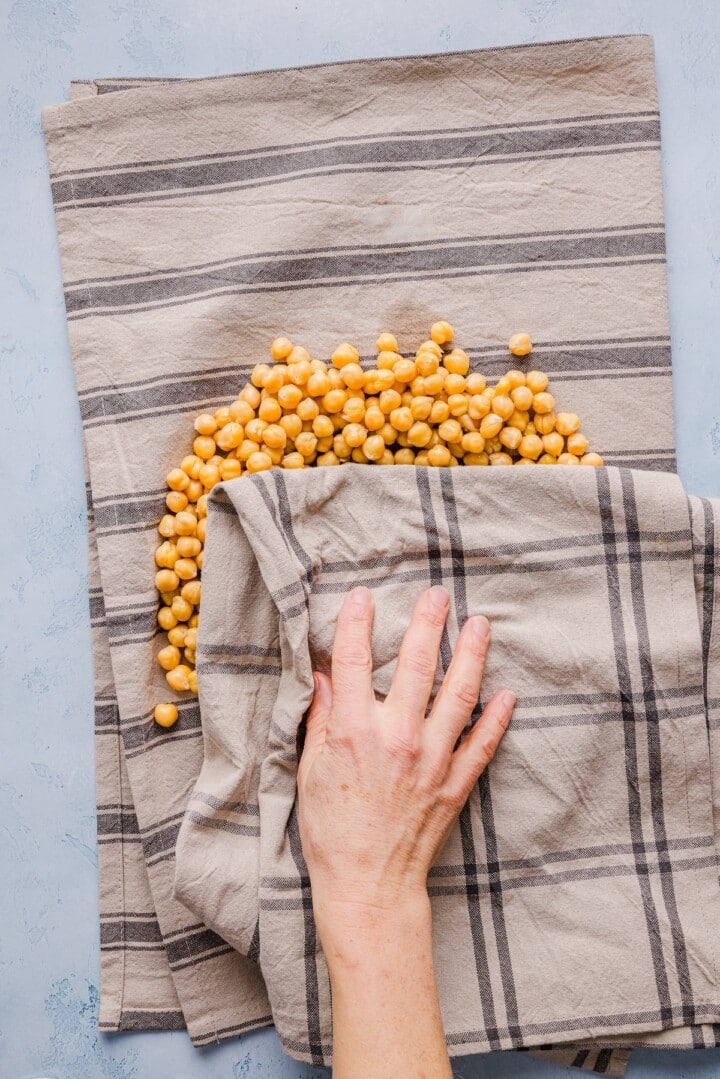 Canned chickpeas being patted dry on a tea towel.