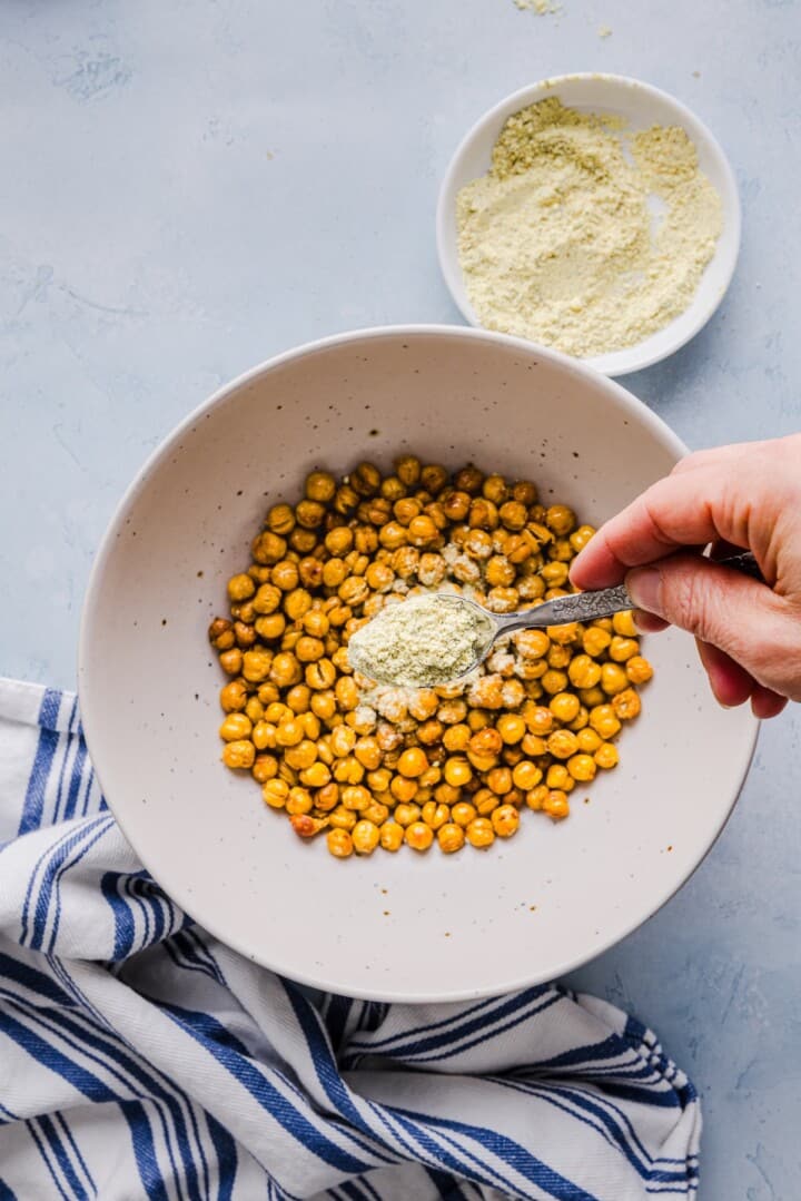 Cooked chickpeas being tossed in powdered popcorn seasoning in a large mixing bowl.
