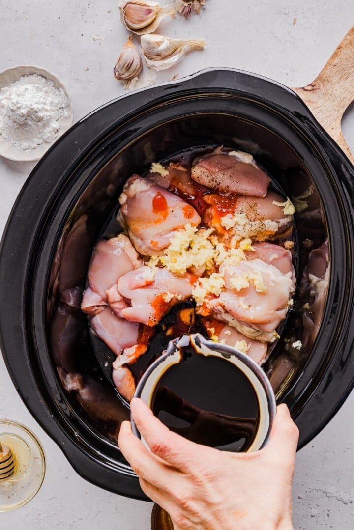Slow cooker chicken being added into a slow cooker.