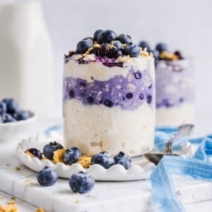 Blueberry cheesecake overnight oats in a glass jar with graham cracker crumbs.