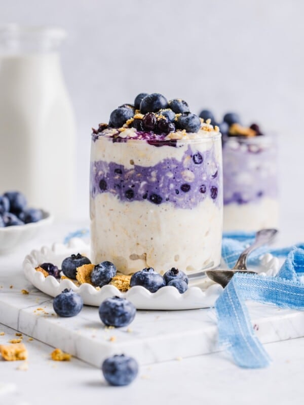 Blueberry cheesecake overnight oats in a glass jar with graham cracker crumbs.
