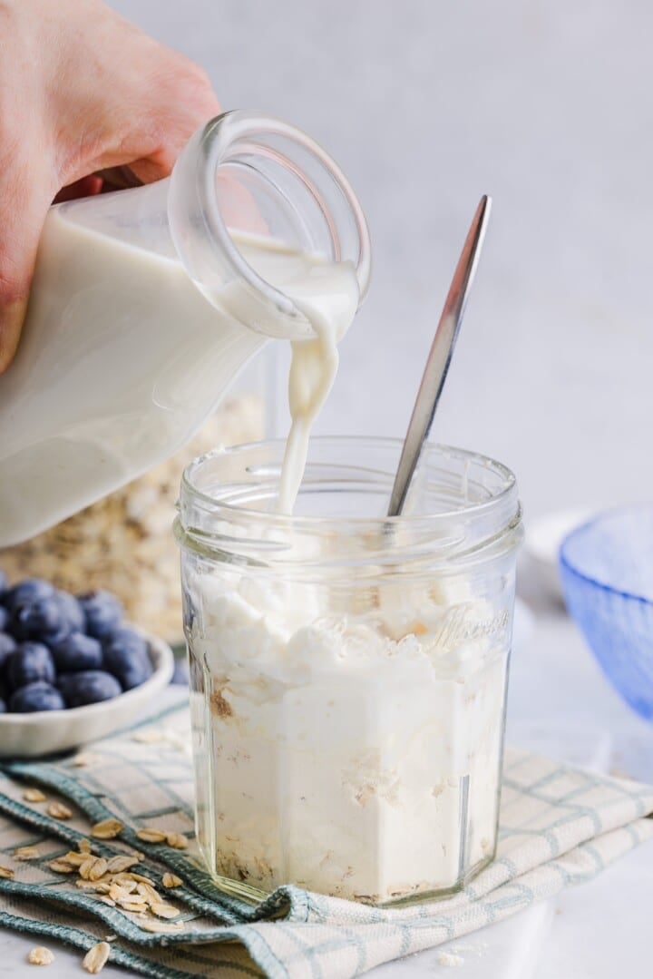 Milk being poured into glass jar with overnight oats ingredients.