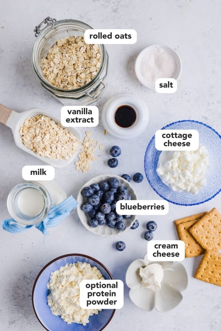 Ingredients for blueberry cheesecake overnight oats displayed in small bowls on a kitchen counter.