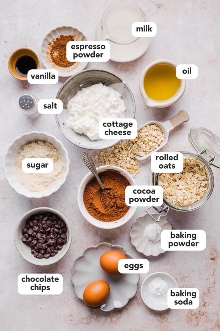 Ingredients for cottage cheese chocolate muffins displayed in small bowls on a marble counter.
