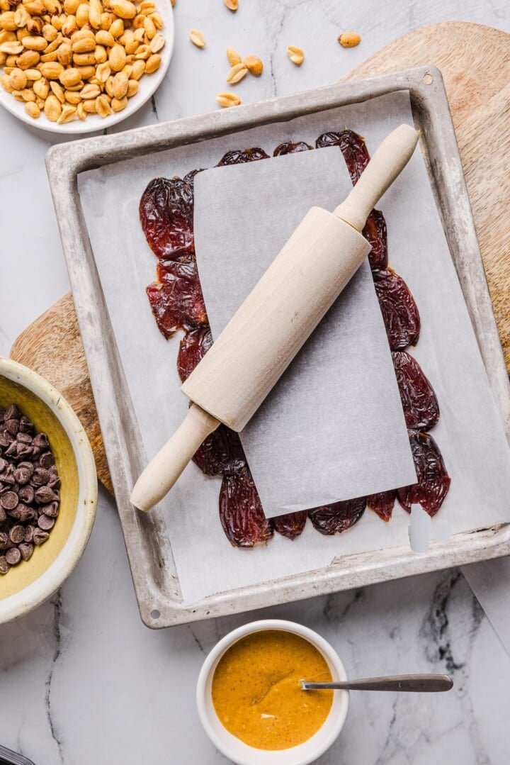 Medjool dates on a parchment-lined sheet pan, being rolled flat with a rolling pin.