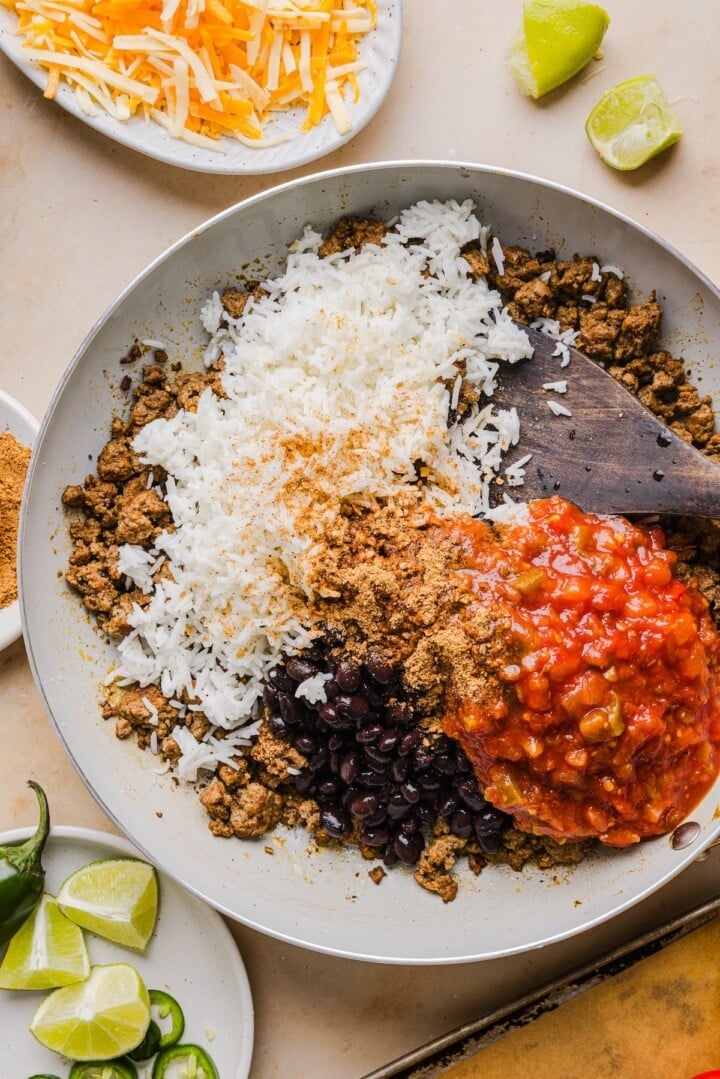 Rice, black beans, salsa, and taco seasoning stirred into cooked ground beef in a pan.