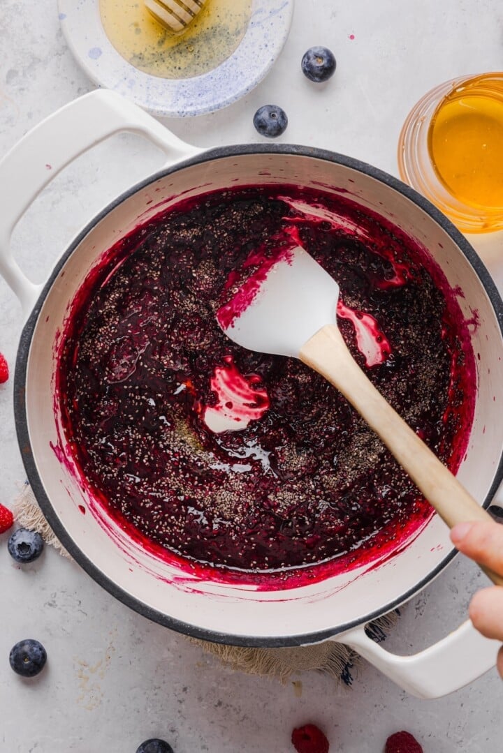 Chia seeds stirred into melted frozen berries in a white pot.