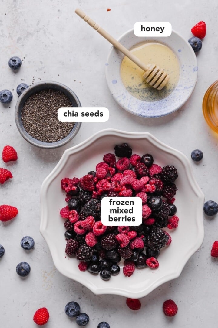 Ingredients for frozen berry chia jam displayed in small bowls on a grey marble counter.