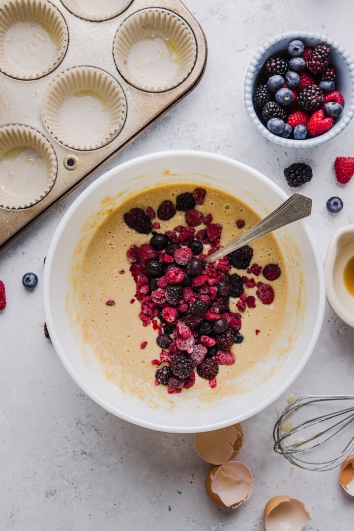 Protein pancake muffin better with frozen berries in a white mixing bowl.