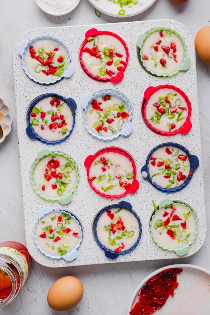 Raw egg white bites in a muffin pan, topped with roasted red pepper and green onion.