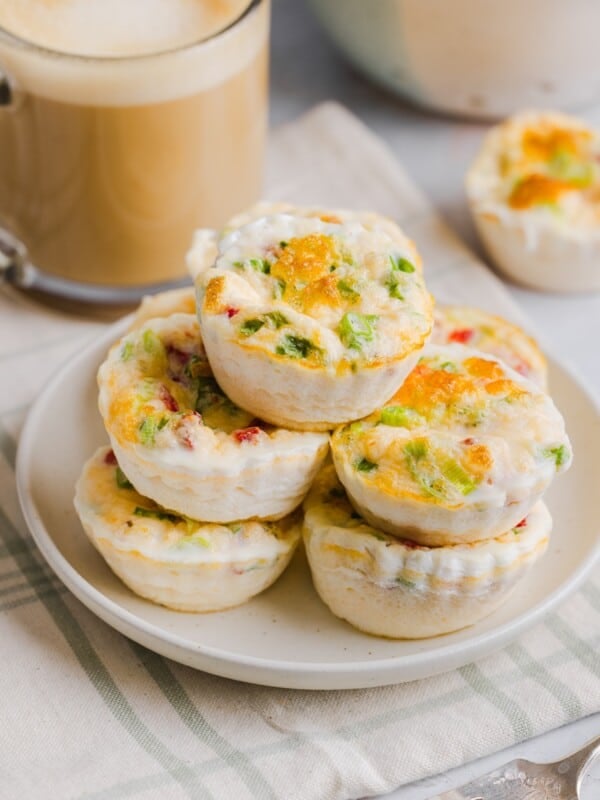 Starbucks egg white bites stacked on a white plate, next to a latte in a glass mug.