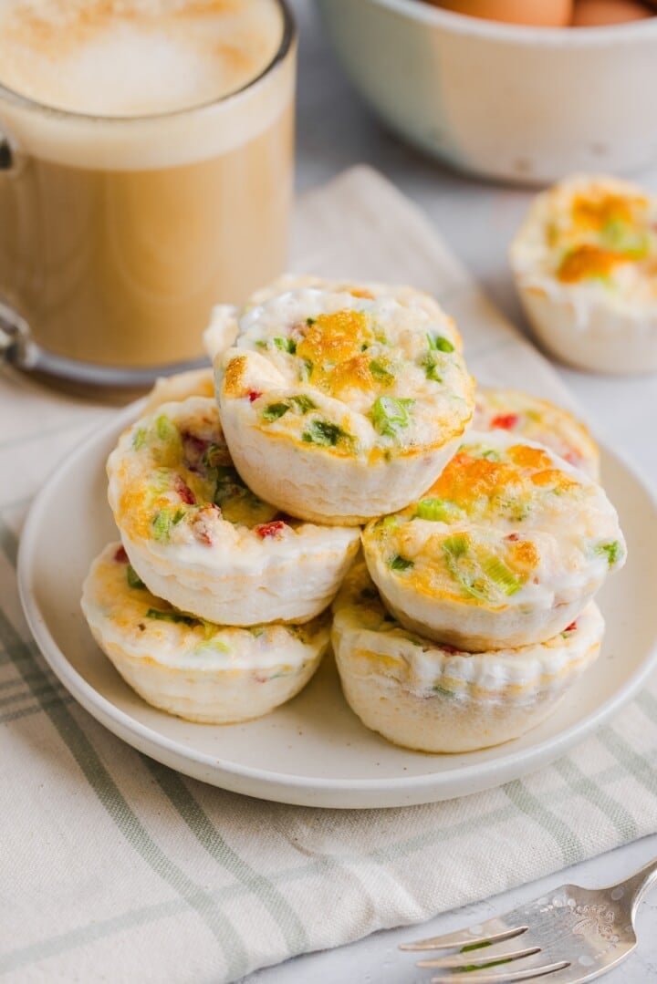 Starbucks egg white bites stacked on a white plate, next to a latte in a glass mug.