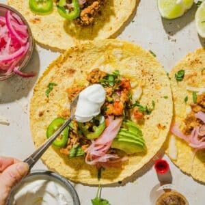 Hand adding toppings to the easy ground turkey tacos.